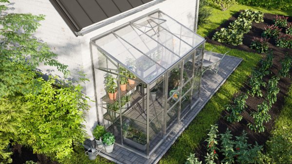 Bright aluminum greenhouse with glass panels on a garden patio, surrounded by lush plants and soil beds, ideal for versatile gardening and plant cultivation.