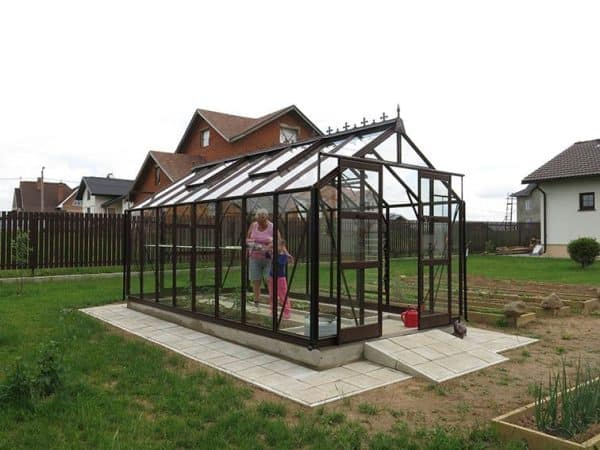 High-quality black metal greenhouse with glass panels, perfect for home gardening and plant cultivation, featuring easy access and a sturdy foundation.