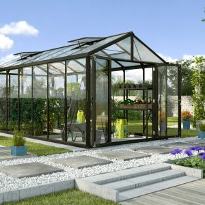 Aluminum and glass greenhouse for optimal plant growth and gardening efficiency in a beautiful landscaped garden setting.