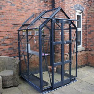 Greenhouse with black frame and glass panels, perfect for gardening and plant protection, situated outside a brick house in a residential garden.
